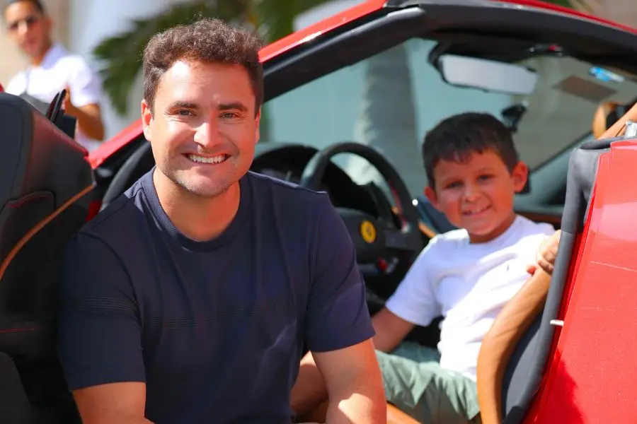Father and son smiling beside a red Ferrari