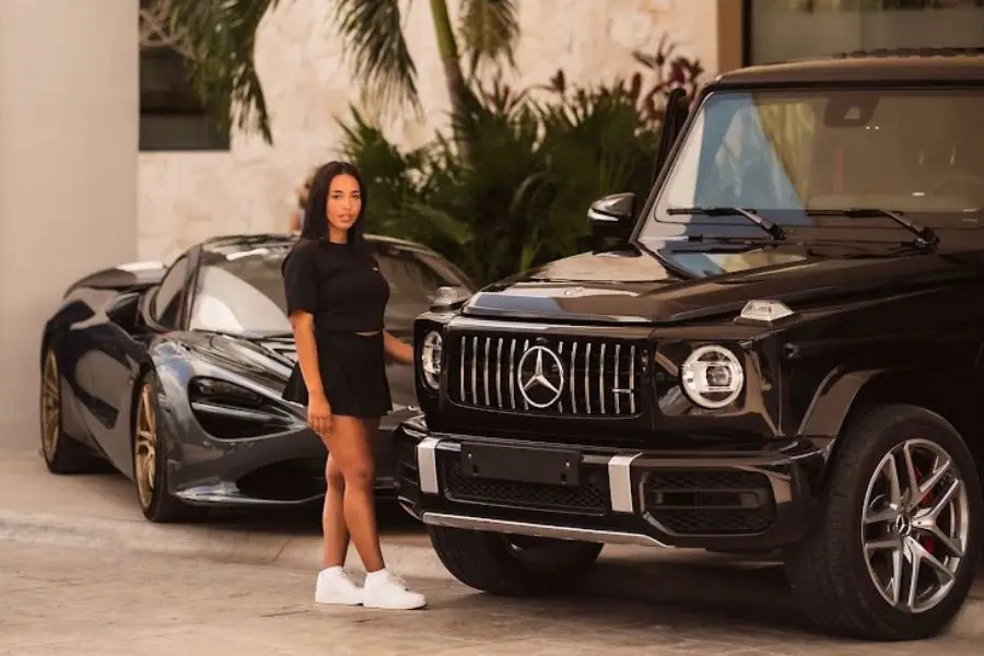 Woman standing between a blue McLaren and a green Mercedes G-Class